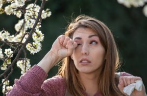 A woman rubbing her eyes due to eye allergies from outside
