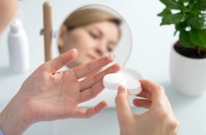 A woman holding a contact lens on her left index finger, and a contact lens case in her right hand