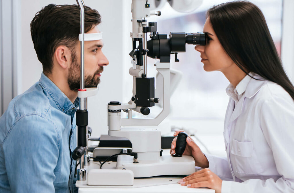 A female doctor ophthalmologist is looking through a slit lamp examining the retina and blood vessels od a make patient.