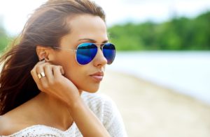 A young woman wearing polarized sunglasses while sitting outside near a river.
