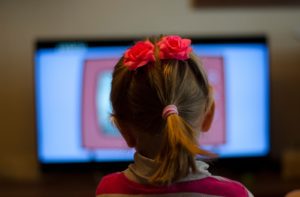 A young girl sitting close to the television screen while watching cartoons.