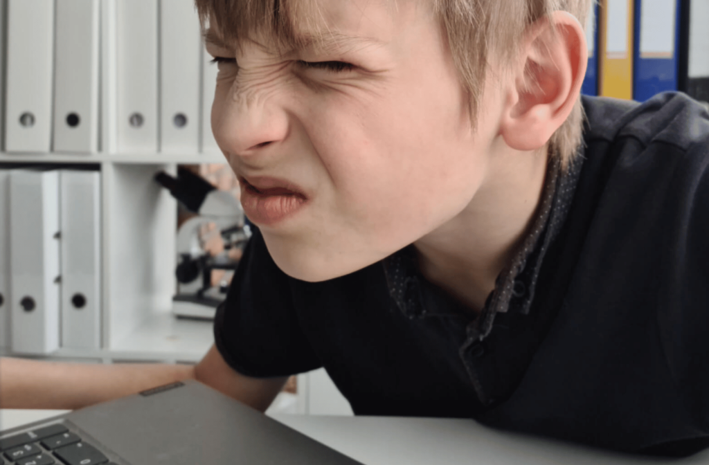 A teenage boy struggling with poor eyesight squints to see his computer screen clearly.
