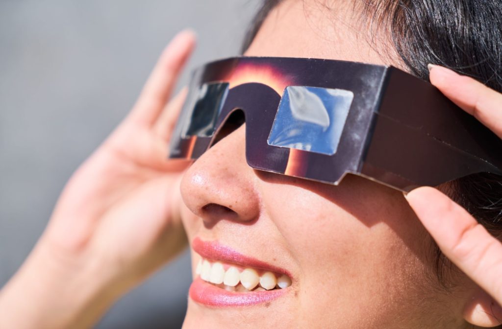 Woman wearing eclipse glasses looking up towards the sky during a solar eclipse.