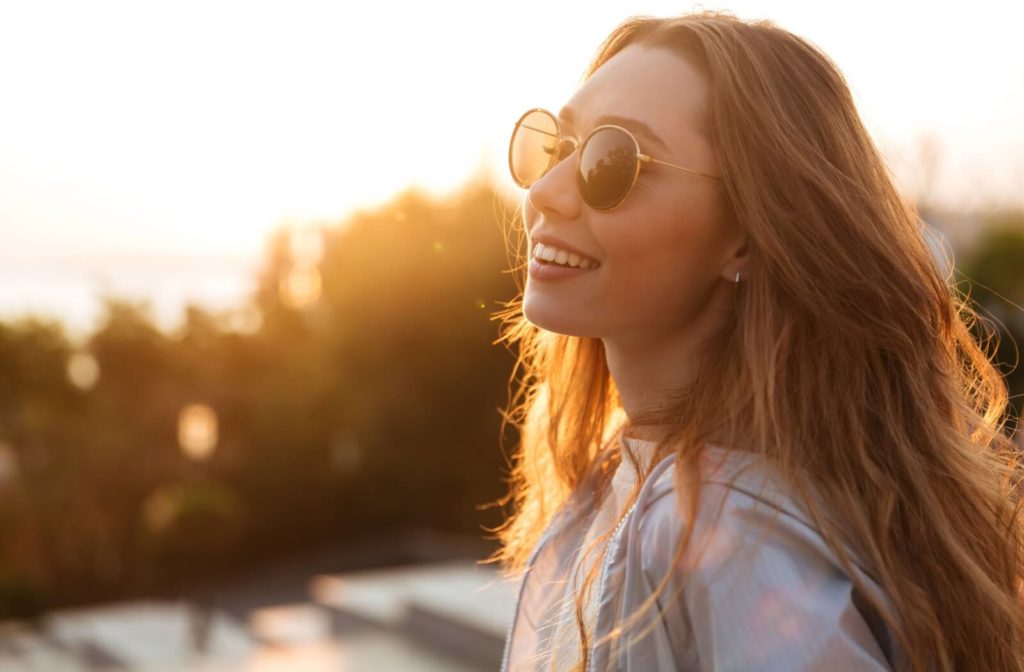 A smiling young woman outdoors wearing sunglasses to prevent eye damage.
