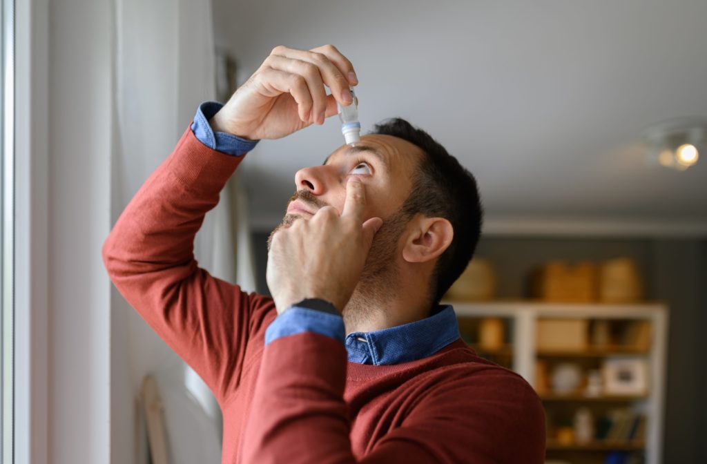 An adult carefully putting eye drops into their left eye to find relief from dry eyes in the winter.