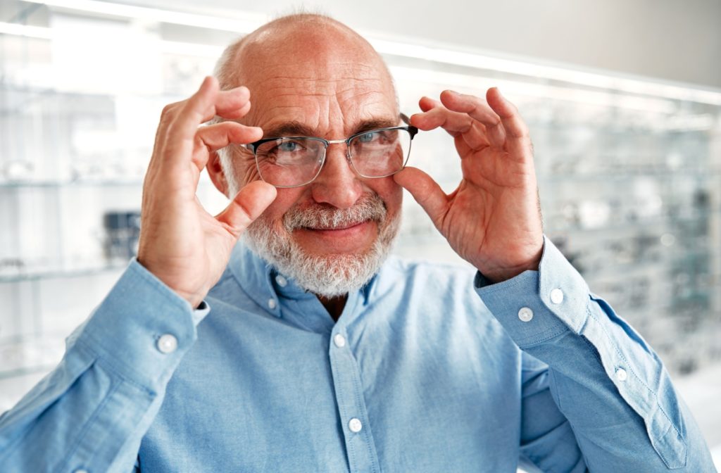 An older adult smiling while trying on a new pair of eyeglasses in an optometry clinic after getting a new prescription.