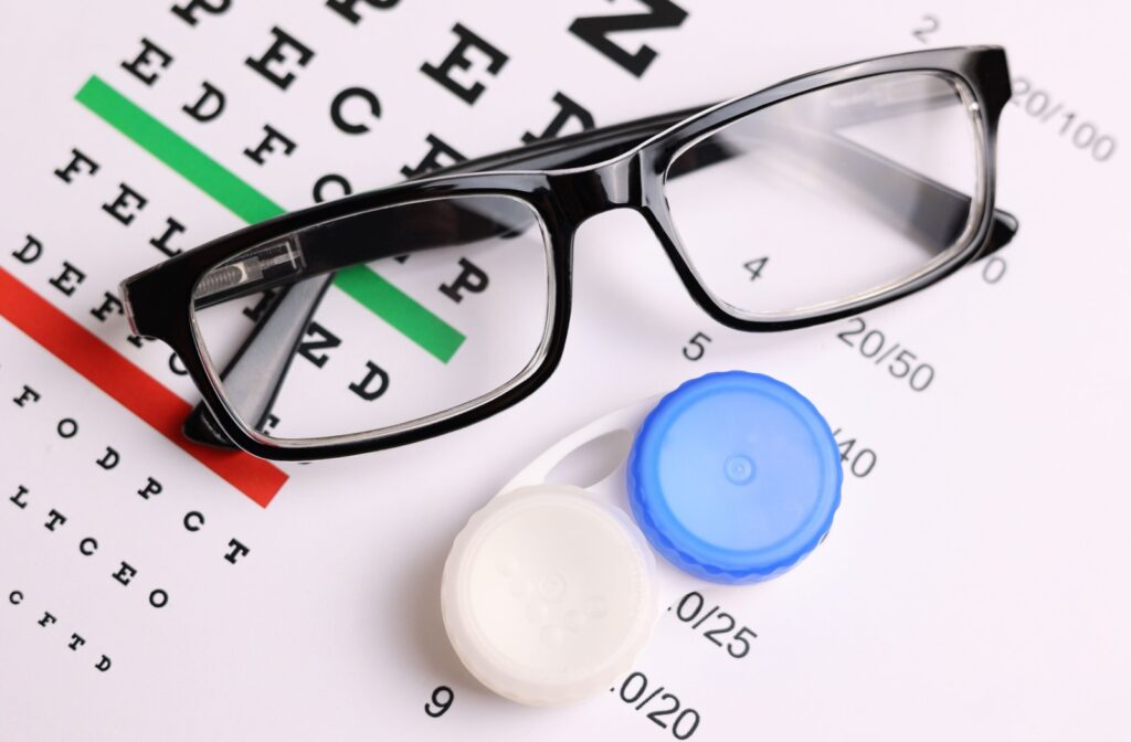 A pair of black eyeglasses and a blue and white contact lens case on top of a vision test chart.