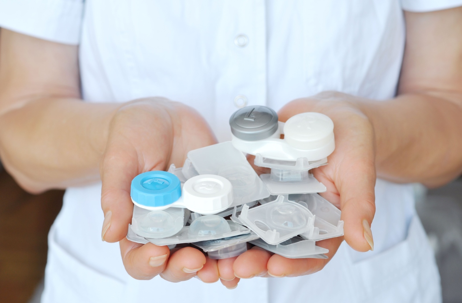 Close-up of a person in a white coat's hands holding contact lens cases.