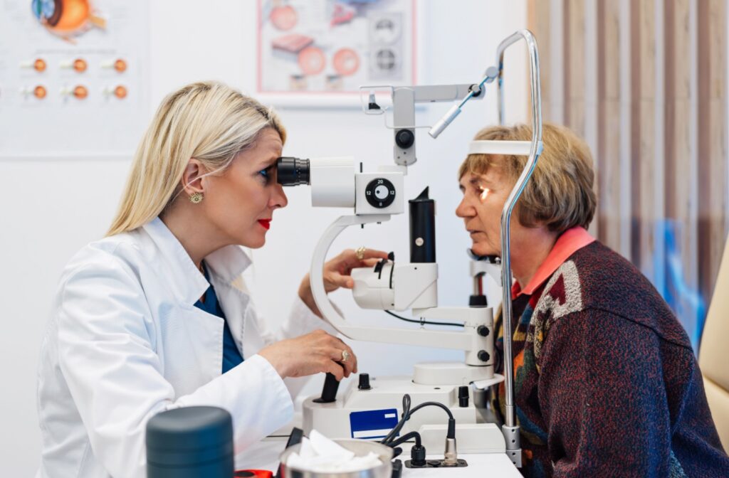 An older adult sits while their optometrist examines their eye with a slit lamp.