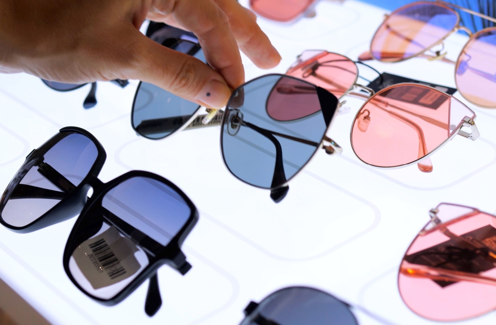 A close-up image of a hand picking sunglasses off of a display rack.