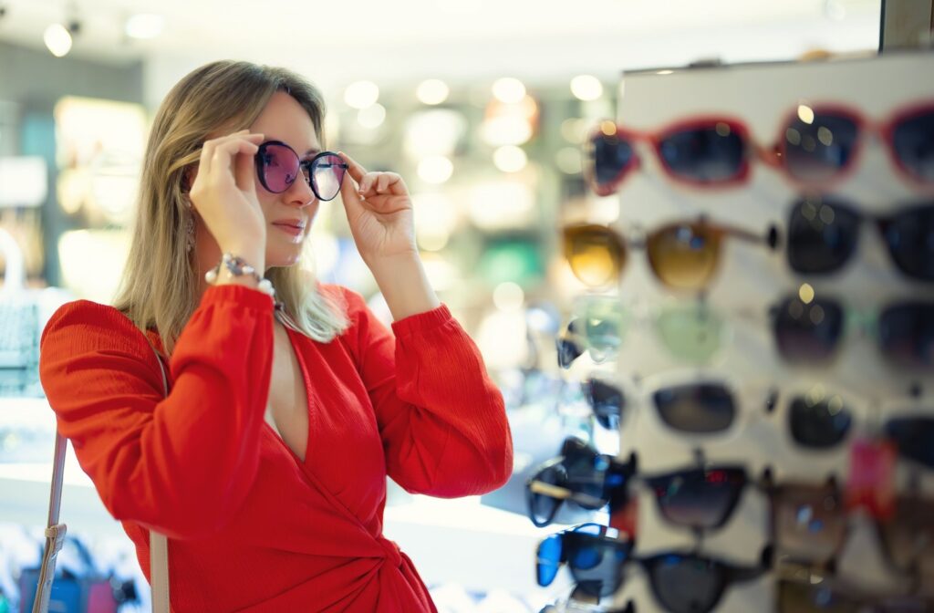 A smiling adult tries on sunglasses in their optometrist's showroom.