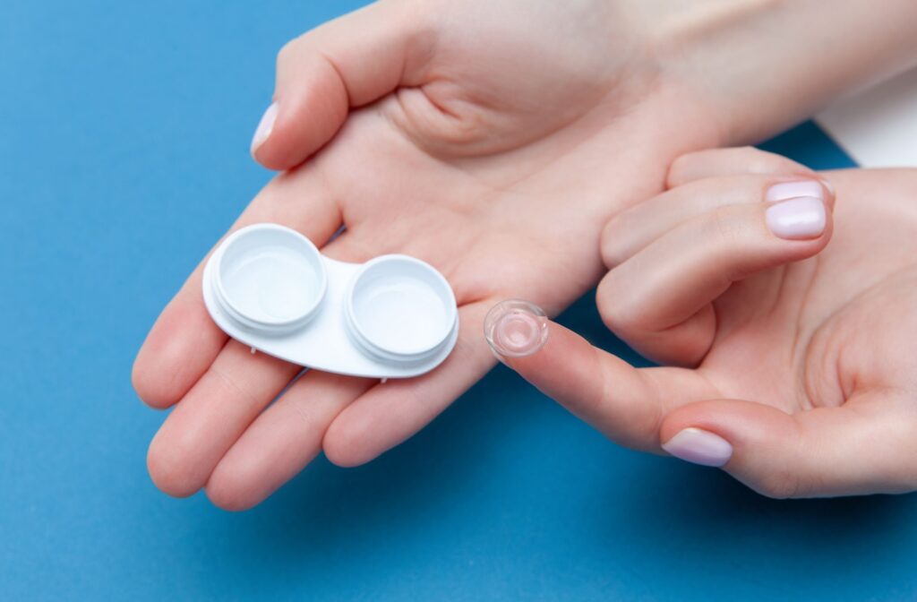 A top-down image of a hand taking a soft contact lens out of its storage case.